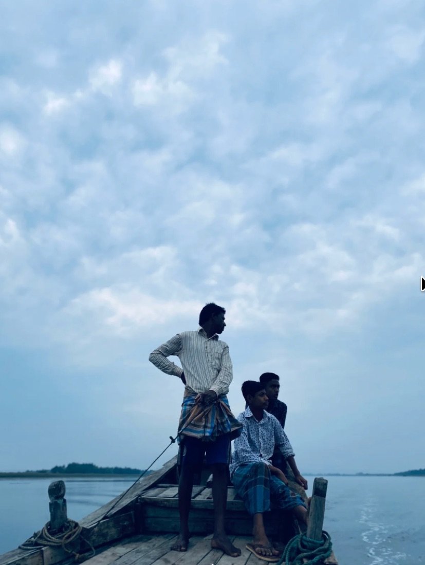 Three people aboard a wooden boat on calm coastal water